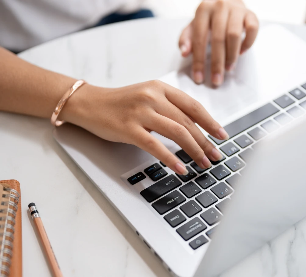 Hands typing on a laptop at a white desk